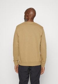 Sweat-shirt marron en tissu doux, avec un col rond et des poignets et ourlet côtelés. Design simple sans motifs ni accents supplémentaires.