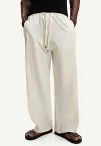 Light beige wide-leg pants with a textured fabric, elastic waistband, and drawstring. Features side pockets and falls to ankle length.