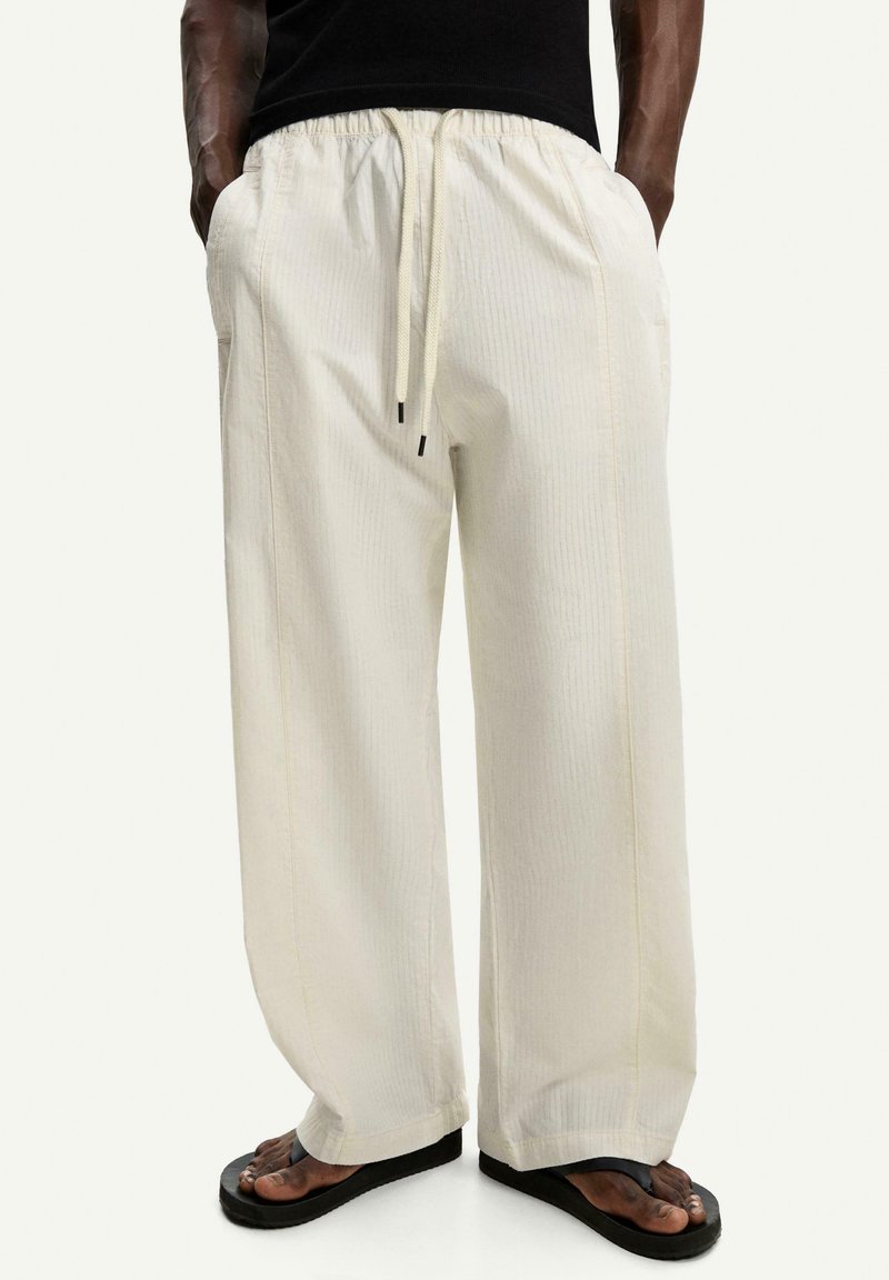 Light beige wide-leg pants with a textured fabric, elastic waistband, and drawstring. Features side pockets and falls to ankle length.