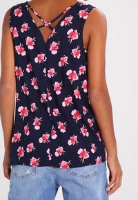 Marineblaues Blumentop mit pinken und weißen Blüten, ausgestattet mit einem V-Ausschnitt und gekreuzten Trägern. Leichter Stoff mit lockerer Passform.