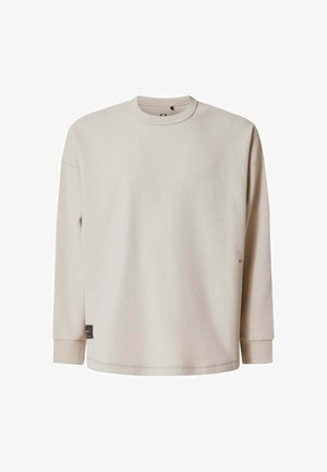 Light beige long-sleeve shirt with a waffle texture, round neckline, and ribbed cuffs. Features a small label on the lower side.