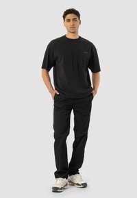 Zwarte t-shirt met korte mouwen en een zak, gecombineerd met zwarte broek en witte sneakers. Casual, moderne pasvorm. Gestructureerde stof, rechte snit.