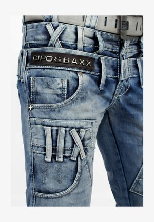 Blauwe denim cargobroek met een zwart logo label, meerdere zakken, textuursteek en unieke banddetails aan de zijkant.
