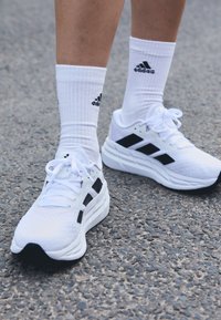Baltas sporta apavus ar melniem akcentiem, teksturētu materiālu un biezu zoli. Saskaņoti ar baltām stumbra zeķēm ar melnu logo.