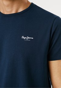 T-shirt in cotone blu navy con scollatura rotonda, maniche corte e logo bianco "Pepe Jeans London" sul lato sinistro del petto.