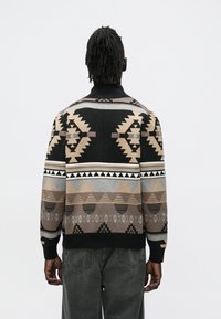 Pleteni pulover z geometrijskim vzorcem v črni, bež in sivi barvi, z dolgimi rokavi, visokim izrezom in rebrastimi manšetami.