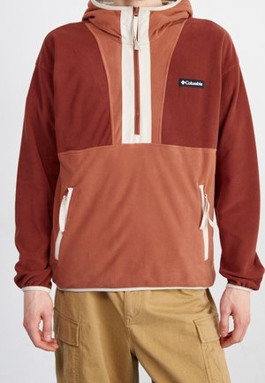 Felpa in pile con zip, rossa e marrone, con cappuccio e design color-block. Presenta una zip verticale centrale e tasche laterali con accenti bianchi.