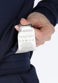 Navy blue fabric with a smooth texture, featuring a care label sewn inside, detailing materials and washing instructions in multiple languages.