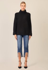 Maglione nero a collo alto a costine con maniche lunghe, abbinato a jeans blu a vita media con dettagli frangiati all'orlo e tacchi neri con cinturini.
