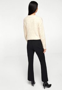 Maglione beige con lavorazione a maglia testurizzata, abbinato a pantaloni neri su misura e stivali con tacco alto. La vista è da dietro.