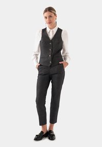 Grijze schotse vest met vijf knopen, gecombineerd met op maat gemaakte grijze broek en een witte overhemd met kraag. Zwarte loafers maken de outfit compleet.