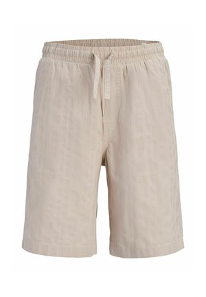 Ung dreng står forfra iført beige kortærmet skjorte med knapper, matchende shorts, lyseblå t-shirt, cremefarvede strømper og brune sko.