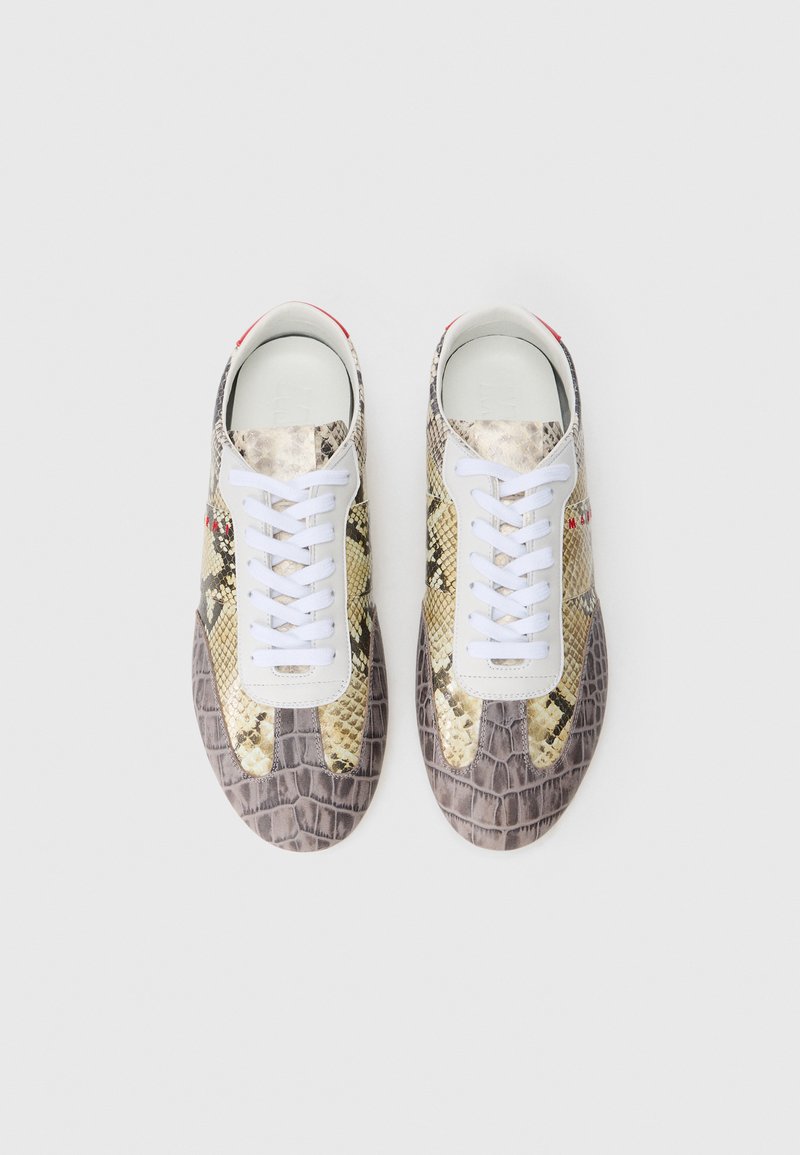 Sneakers med python- og krokodillemønster i beige og grå, der har hvide snørebånd og en hvid tunger med en rød accent på hælen.