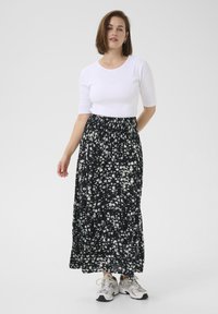 Jupe maxi noire avec imprimé floral blanc, en tissu doux, forme évasée, taille élastique, associée à un haut ajusté blanc et des baskets.