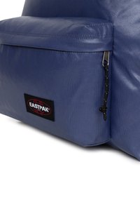 Zaino Eastpak blu con tessuto testurizzato, caratterizzato da una tasca con zip e un'etichetta nera. Finitura liscia con cuciture resistenti.