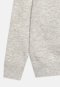 Manga de sudadera gris con una tela suave y texturizada, con un puño acanalado y un sutil patrón jaspeado que añade profundidad.