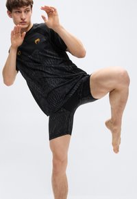 Μαύρο αθλητικό σορτς και αντίστοιχο κοντομάνικο τοπ, με υφή σχεδίου και μικρό χρυσό λογότυπο, κατάλληλα για ενεργό ντύσιμο.