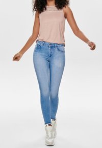 Ljusrosa ärmlös topp med spetsdetaljer, matchad med ljusblå skinny jeans. Bärs med vita sneakers. Enkelt, avslappnat outfit.