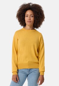 Maglione giallo a maglia con scollatura tonda e polsini a coste, abbinato a jeans denim azzurri. Texture uniforme e vestibilità rilassata.