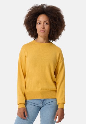 Geel gebreide trui met een ronde hals en geribbelde manchetten, gecombineerd met lichtblauwe denim jeans. Even textuur en een ontspannen pasvorm.