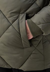 Zielona pikowana kurtka z przeszyciami w kształcie rombów, boczną kieszenią i elastycznymi mankietami w kontrastowym kolorze. Gładka, lekka tkanina.