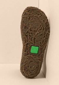 Suela de un zapato marrón con un patrón texturizado parecido a ramas y un logo cuadrado verde con una rana en el centro.