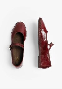 Zapatos de charol burdeos estilo Mary Jane con puntera redonda, tira elástica y costura texturizada a lo largo de la suela. Acabado suave y liso.