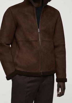 Homme portant une veste zippée en daim brun foncé avec une bordure en peau lainée aux poignets et à l'ourlet, associée à un pantalon sombre.