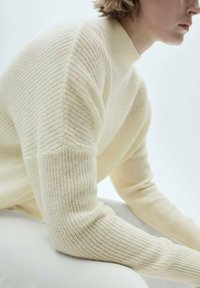 Maglione lavorato a maglia color crema con collo alto, caratterizzato da un motivo a coste testurizzato e spalle leggermente scese.