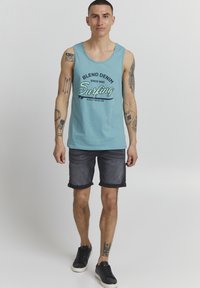 Svijetloplavi majica na bretele s crnim grafičkim tekstom "Blend Denim Surfing" i tamnoplave traperice. Uključuje prevrnuti rub i crne tenisice.