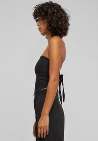 Svart strapless topp laget av glatt stoff, med en tettsittende design og en knytedetalj bak. Bæres med matchende svarte bukser.