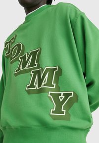 Zelená mikina s výrazným, vrstveným nápisem v bílé a tmavě zelené barvě, s klasickým kulatým výstřihem a žebrovanými manžetami.