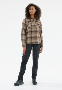 Gepofte shirt in bruin met donkerbruin en roestkleurige accenten; twee borstzakken. Gecombineerd met zwarte broek, met gestructureerde stof en laarzen.