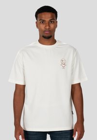 Camiseta blanca de manga corta hecha de algodón, con un pequeño diseño bordado de un personaje en la parte izquierda del pecho.
