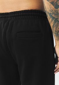 Pantalones de chándal negros con cintura elástica, textura suave y un pequeño bolsillo trasero con detalle de costura.