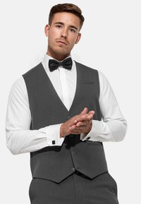 Gilet gris avec un col en pointe, cinq boutons et des poches latérales. Porté sur une chemise blanche à poignets français et un nœud papillon noir.