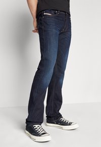 Mörkblå denimjeans med rak benstil, med orange sömmar, framfickor och bärs med svarta höga sneakers.