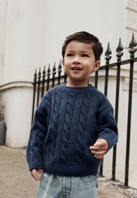 Marineblauwe kabelgebreide trui met geribbelde ronde hals en lange mouwen, gecombineerd met licht denim jeans. Eenvoudige textuur en ontspannen pasvorm.