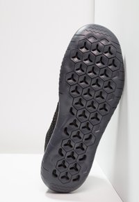 Suela de zapatilla atlética negra con un patrón de agarre texturizado de formas hexagonales. Bordes lisos y una ligera curvatura en la punta.