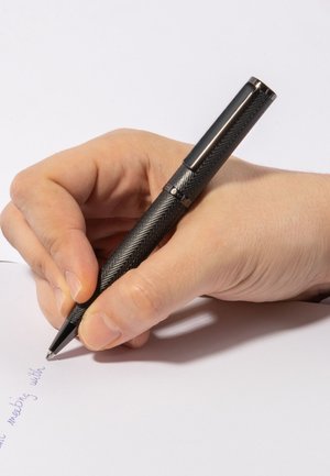Schwarz strukturierter Stift mit einem Fischgrätenmuster, der in einer Hand gehalten wird und auf weißem Papier schreibt. Der Stift hat ein glänzendes silbernes Band in der Nähe des Griffs.
