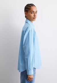 Camicia a righe blu e bianche con maniche lunghe, vestibilità comoda e colletto a punta, realizzata in tessuto leggero.