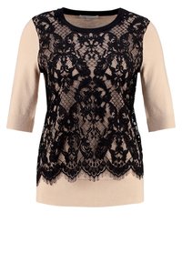 Spetsöverdel med en svart spetstoppöverdrag med blommönster, beige stickade ärmar och rund halsringning. Hemsömmen är vågig.
