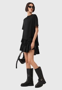 Zwarte oversized t-shirt jurk met een gerimpelde zoom, korte mouwen, gecombineerd met kniehoge zwarte laarzen en een kleine zwarte handtas.