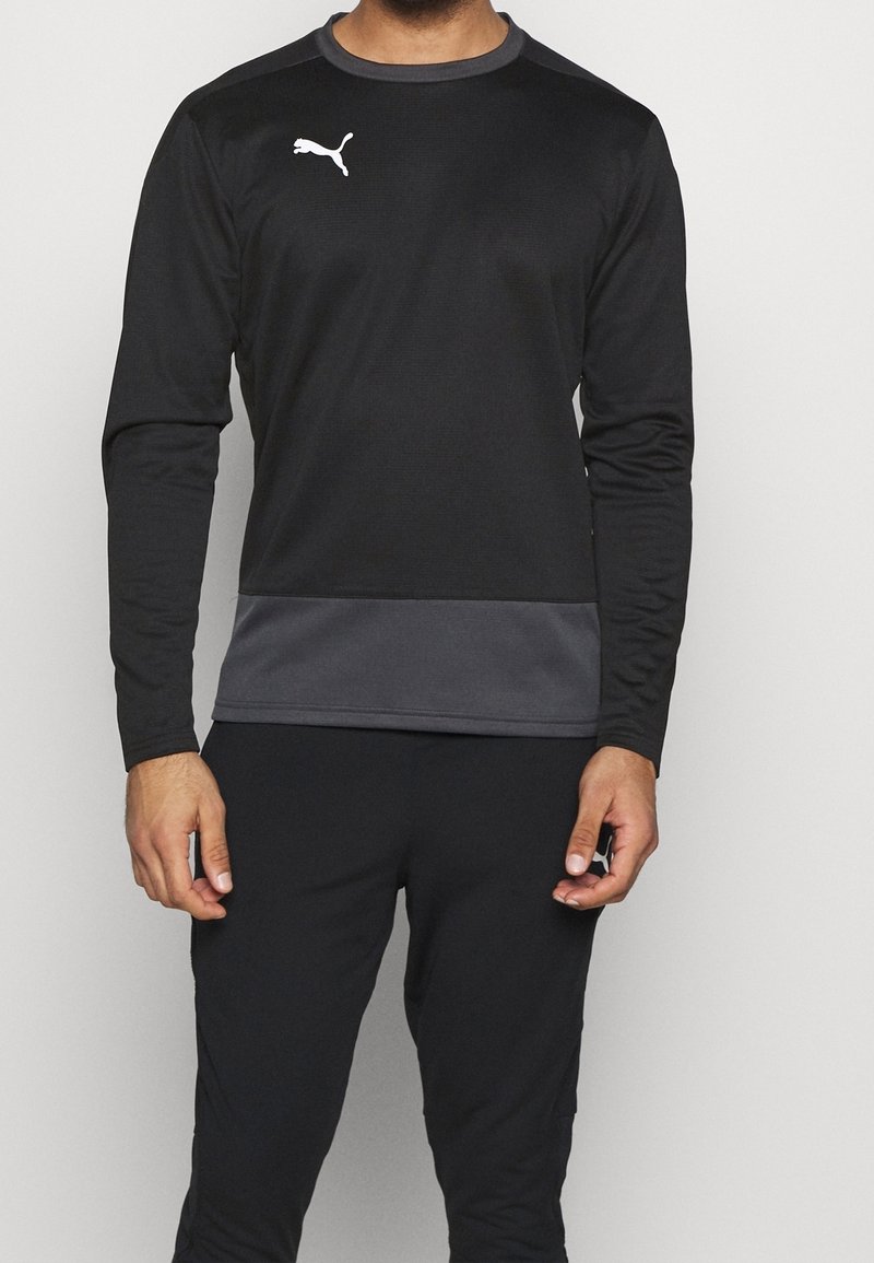 Homme portant un maillot de sport Puma noir à manches longues avec une bande gris foncé à la taille et un pantalon noir assorti.