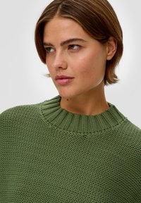 Groene trui met een geribbelde, hoge hals, textuur gebreide stof en een licht losse pasvorm. Het ontwerp heeft een subtiel, geweven patroon.
