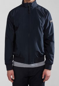 Marine let term buks med lynlåslukning, ribbede manchetter og kant, med et logo patch på venstre bryst og glat tekstur.