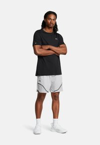 Camiseta atlética negra de mangas cortas, combinada con pantalones cortos grises claros con un diseño geométrico y acentos en negro.