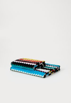 Dos tejidos doblados con patrones en zigzag en colores vibrantes que incluyen azul, negro, rojo y amarillo, con un aspecto texturizado y tejido.