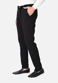 Pantaloni di cotone neri con vestibilità slim, caratterizzati da tasche laterali e vita con cordoncino. Abbinati a scarpe slip-on nere.
