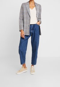 Szaro-niebieska marynarka w kratę na kremowej dzianinowej bluzce, zestawiona z luźnymi niebieskimi dżinsami i beżowymi sneakersami. Casualowy, warstwowy strój.